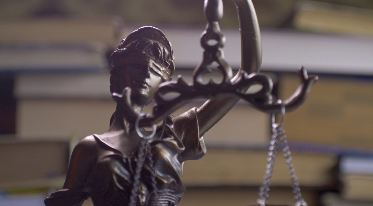 Close-up of a justice statue holding scales, with books blurred in the background.